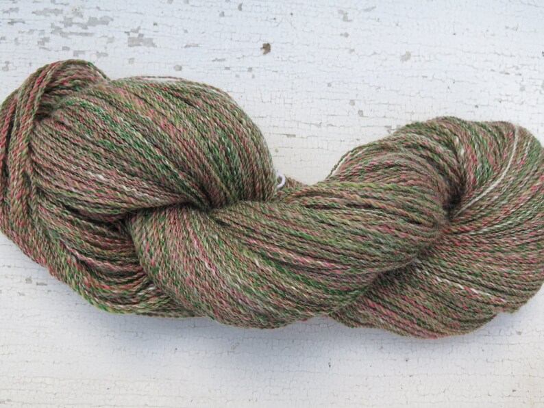 May include: A skein of yarn in a green, pink, and white colorway. The yarn is made of wool and is suitable for knitting or crocheting.
