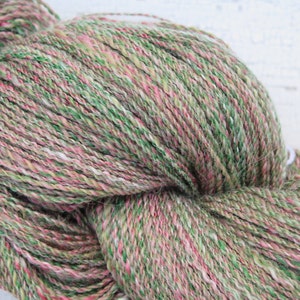 May include: A skein of yarn in shades of green, pink, and white. The yarn is a blend of wool and silk, and it has a soft, fuzzy texture.
