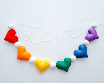 May include: A rainbow felt heart garland with white pom poms and the word "love" spelled out in white string.