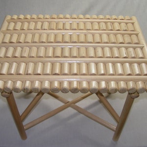 May include: A wooden folding table with a unique top made of small, round wooden dowels arranged in a grid pattern. The table is made of natural wood and has a light brown finish.