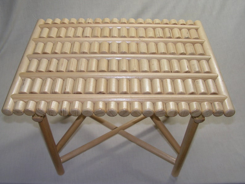 May include: A wooden folding table with a unique top made of small, round wooden dowels arranged in a grid pattern. The table is made of natural wood and has a light brown finish.