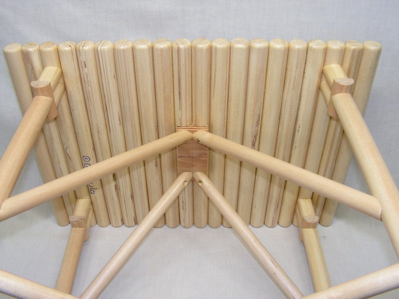 May include: A wooden stool with a slatted top and a triangular base. The stool is made of natural wood and has a rustic look.