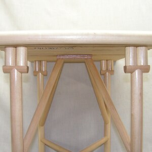 May include: A wooden table with a slatted top and a unique, intricate base made of multiple wooden pieces. The table is made of light-colored wood and has a natural finish.