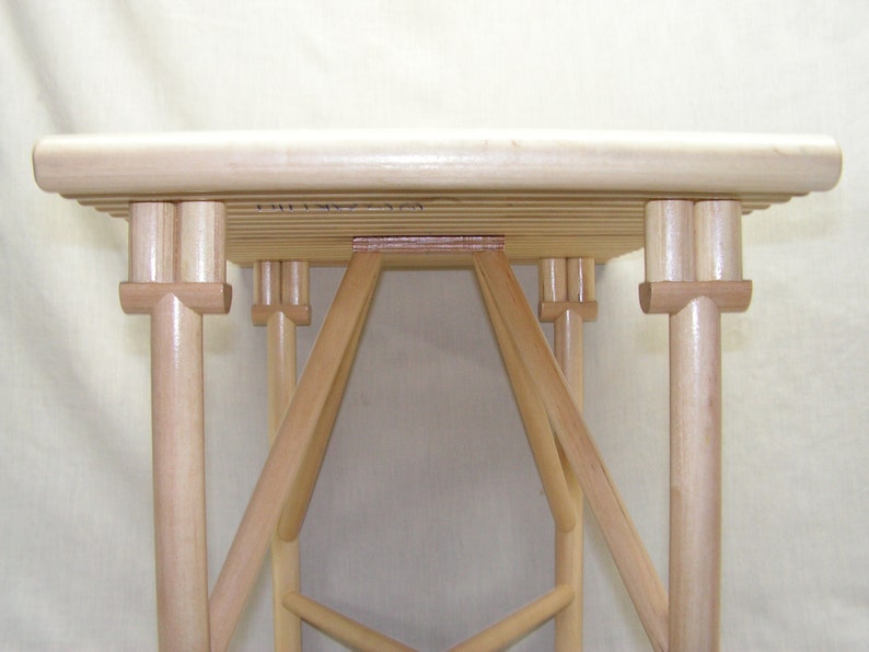 May include: A wooden table with a slatted top and a unique, intricate base made of multiple wooden pieces. The table is made of light-colored wood and has a natural finish.