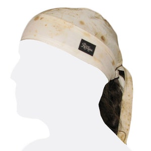 Może przedstawiać: Biała bandana z brązową plamą i czarną etykietą z napisem "Roxisa". Bandana jest zawiązana wokół głowy osoby z brązowymi włosami.