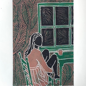 Linoprint 'Sunday morning' | girl, woman sitting at a table by the window. She drinks coffee, tea and still has her shoes off.