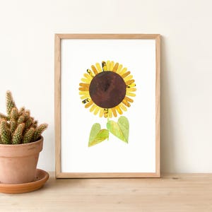 May include: A framed print of a sunflower made from paper. The sunflower is yellow and brown with green leaves. The print is on a white background.