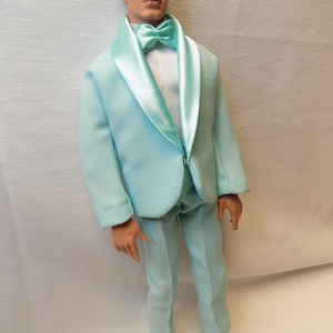 May include: A light blue suit with a satin lapel and a matching bow tie. The suit is made of a textured fabric and has a classic fit.