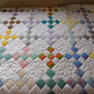 May include: A white quilt with a patchwork design. The quilt is made up of squares of different colors and patterns, including floral, plaid, and polka dot. The quilt is quilted with a swirl pattern.
