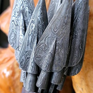 May include: Close-up of a bundle of arrowheads with a unique, patterned design. The arrowheads are made of a gray metal with a swirling, wood-grain-like texture. They are held in a dark brown quiver, suggesting a hunting or archery theme.