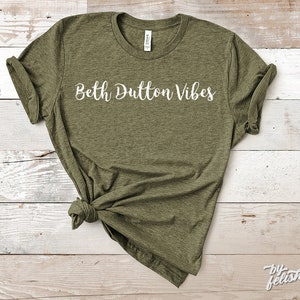 Könnte beinhalten: Ein grünes T-Shirt mit dem Text "Beth Dutton Vibes" in weißen Buchstaben.