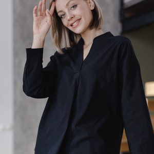 Pode incluir: Uma mulher vestindo uma camisa preta de manga comprida com gola em V e calças pretas.