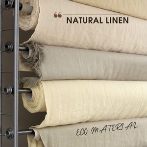 May include: Rolls of natural linen fabric on a metal rack. The fabric is a light beige colour and has a slightly textured surface. The text "NATURAL LINEN" and "ECO MATERIAL" is visible on the fabric.