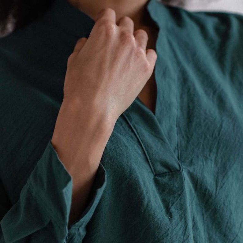 May include: A close-up of a person wearing a dark green long-sleeved shirt with a V-neck.