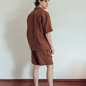 May include: A person wearing a brown linen short-sleeved shirt and matching shorts. The person is standing with their back to the camera and looking over their shoulder.