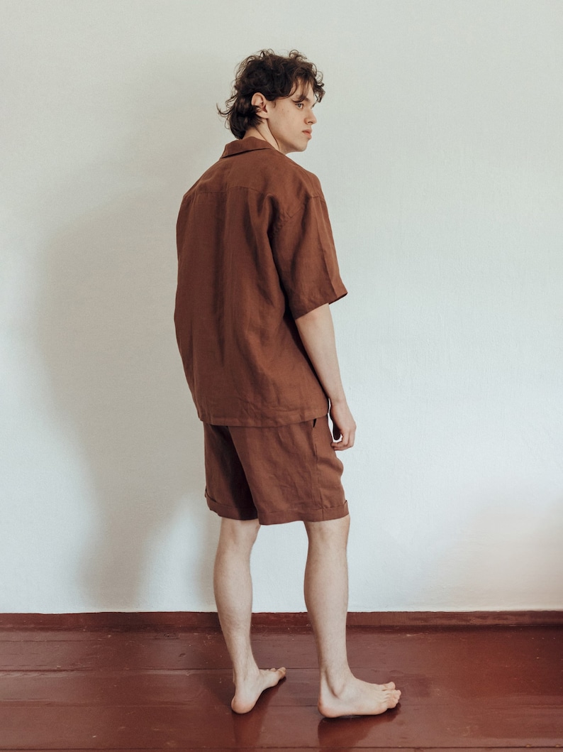 May include: A person wearing a brown linen short-sleeved shirt and matching shorts. The person is standing with their back to the camera and looking over their shoulder.