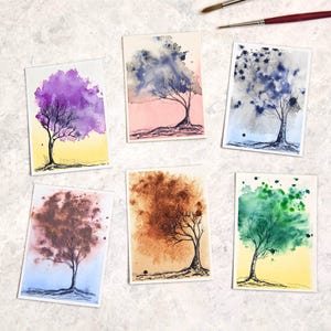 Può includere: Cinque dipinti rettangolari ad acquerello di alberi con colori del fogliame distinti, tra cui viola, blu, marrone, arancione e verde, disposti con due pennelli sottili. Ogni dipinto presenta una silhouette di albero disegnata a inchiostro.