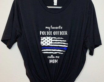 May include: Black t-shirt with a white graphic that says "My favorite police officer calls me mom" with a blue line American flag design.