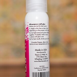 May include: A white bottle of all-purpose craft glue with a clear spray nozzle. The label includes instructions and the text "Made in USA". The bottle is non-toxic and conforms to ASTM D-4236 standards.