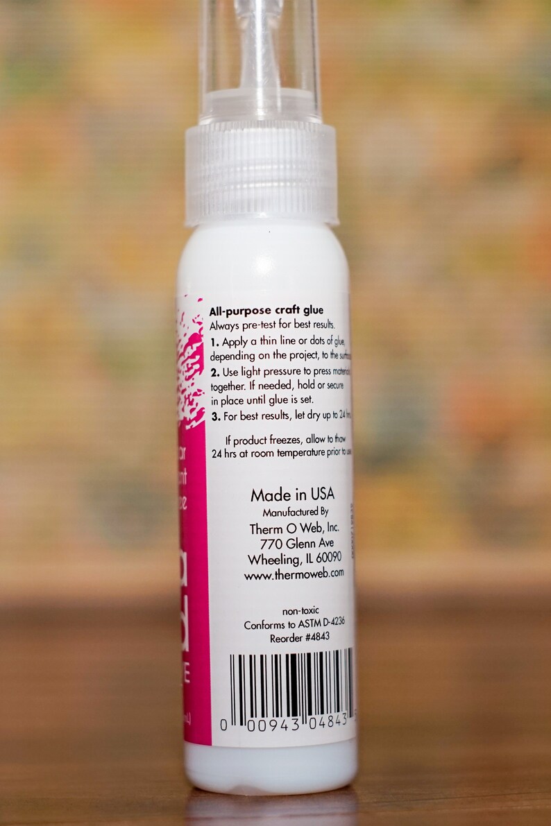 May include: A white bottle of all-purpose craft glue with a clear spray nozzle. The label includes instructions and the text "Made in USA". The bottle is non-toxic and conforms to ASTM D-4236 standards.