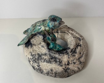 May include: A ceramic sculpture of two blue and green birds perched on a white, textured, circular base.