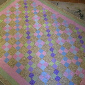 May include: A patchwork quilt with a checkered pattern in shades of pink, green, purple, and blue. The quilt is made of various floral patterned fabrics.