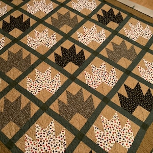 May include: A quilt with a pattern of brown, green, and white leaves. The quilt is made of different fabrics and has a quilted texture.