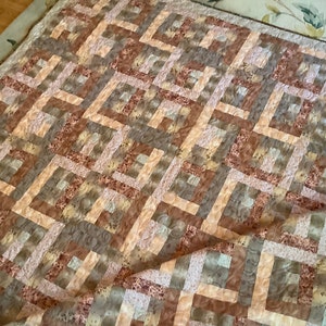 May include: A quilt with a geometric pattern in shades of brown, beige, and pink. The quilt is made of fabric with a floral print.