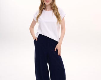 May include: A white short-sleeved t-shirt with a round neckline paired with loose-fitting navy blue trousers. The trousers feature a high-waisted design with side pockets and a wide-leg silhouette. The outfit is completed with white athletic sneakers.