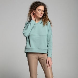 May include: A light blue hooded sweatshirt with a relaxed fit and long sleeves. The model is wearing the sweatshirt with brown faux leather trousers and white trainers.
