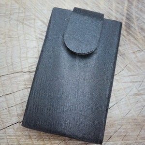 Peut inclure: Une pochette en tissu noir avec une fermeture à rabat. La pochette est conçue pour contenir un petit appareil électronique, comme un téléphone ou une tablette.