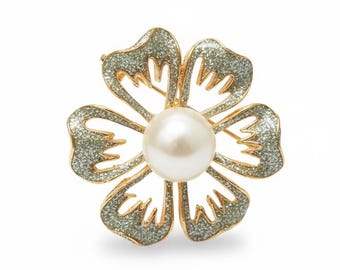 May include: A gold-toned flower brooch with a large, round, white pearl center. The flower petals are outlined in gold and filled with a shimmering, glittery silver material. The brooch has a pin backing.