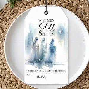 May include: A white gift tag with a black string, featuring watercolor art of the Three Wise Men. The tag reads "Wise Men Still Seek Him" and "Wishing You a Merry Christmas!" with a signature at the bottom. The tag is on a white plate.