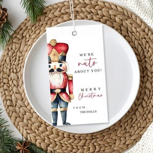 May include: A white gift tag with a watercolor illustration of a nutcracker. The tag says "We're nuts about you! Merry Christmas from the Halls."