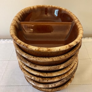 May include: A stack of eight brown and cream divided ceramic bowls. The bowls have a glazed finish and a unique speckled pattern.