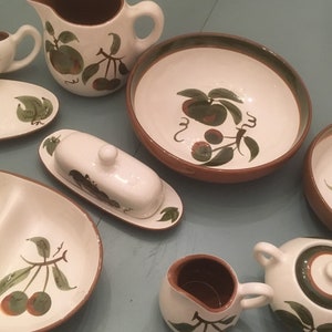 May include: A set of vintage ceramic dishes with a brown and green cherry motif. The set includes a creamer, sugar bowl, butter dish, two bowls, a gravy boat, and a serving dish.