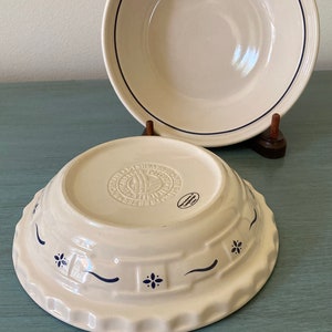 May include: Two white ceramic pie plates with blue trim. The smaller plate has a blue and white floral design and the larger plate has a single blue line around the rim.