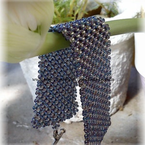 Könnte beinhalten: Nahaufnahme eines Armbands aus irisierenden blauen und violetten Perlen. Das Armband ist in einem Kettenhemdmuster gewebt und hat einen silbernen Verschluss.