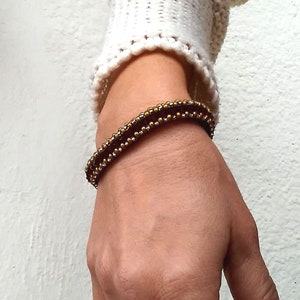 Könnte beinhalten: Ein goldfarbenes und rotes Perlenarmband, das an einem Handgelenk getragen wird.