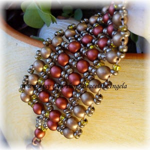 May include: A multi-strand bracelet made of brown, gold, and silver beads. The bracelet is woven in a pattern that creates a geometric design. The bracelet is on a light brown surface.