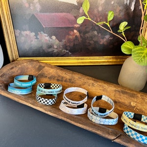 May include: A wooden bowl filled with colorful woven wristbands with inspirational messages, including "I can do all things through Christ" and "Through Christ I can do all things".