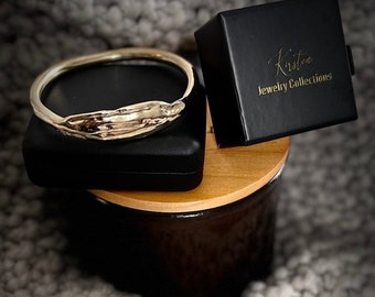 May include: A silver bangle bracelet with an organic, wave-like design. The bracelet is displayed in a black box with the text "Kristen Jewelry Collections".
