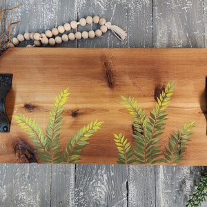 May include: A wooden serving tray with black metal handles. The tray is painted with a green and yellow fern design.