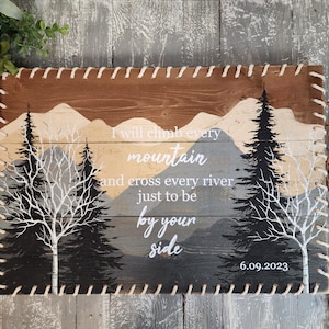 May include: A wooden sign with a mountain landscape and trees painted on it. The sign has a rope border and the text "I will climb every mountain and cross every river just to be by your side 6.09.2023".