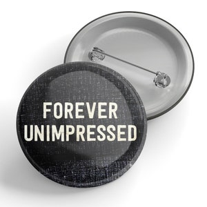 以下が含まれることがあります： テクスチャ加工された背景に「FOREVER UNIMPRESSED」というテキストが書かれた白黒のボタンです。