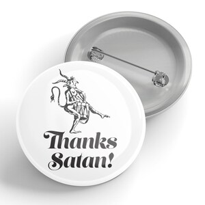 Puede incluir: Un botón blanco con una ilustración en blanco y negro de un diablo tocando un tambor. El texto "Thanks Satan!" está escrito en letras cursivas negras.