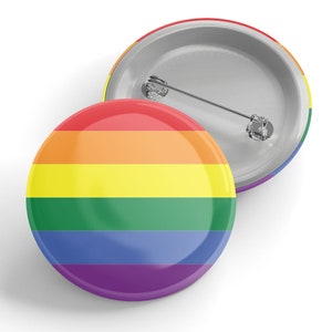 Puede incluir: Un botón de solapa redondo con una bandera del orgullo arcoíris. El botón es redondo y tiene un acabado brillante.