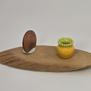May include: A wooden oval-shaped tray with a brown penny and a small yellow and green ceramic pot. The penny is propped up on a small white base. The pot has a ruffled green rim.