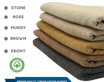 May include: A stack of folded Turkish cotton scarves in various colors: stone, rose, muddy, brown, and ebony. The image includes text indicating the scarves are handmade and made of premium quality cotton.