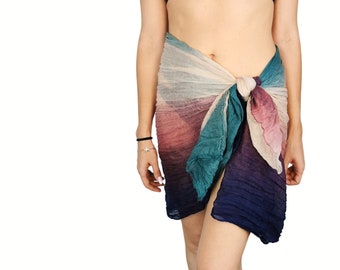 May include: A colorful ombre sarong tied around the waist. The sarong is made of a sheer fabric and features shades of pink, blue, green, and white.
